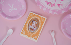 Sena Juo badge in its orange lace-patterned backing card on a pink table with tableware (props not included)