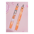Front and back of the China Kuramoto ribbon keychain: illustration with signature, and the name China Kuramoto