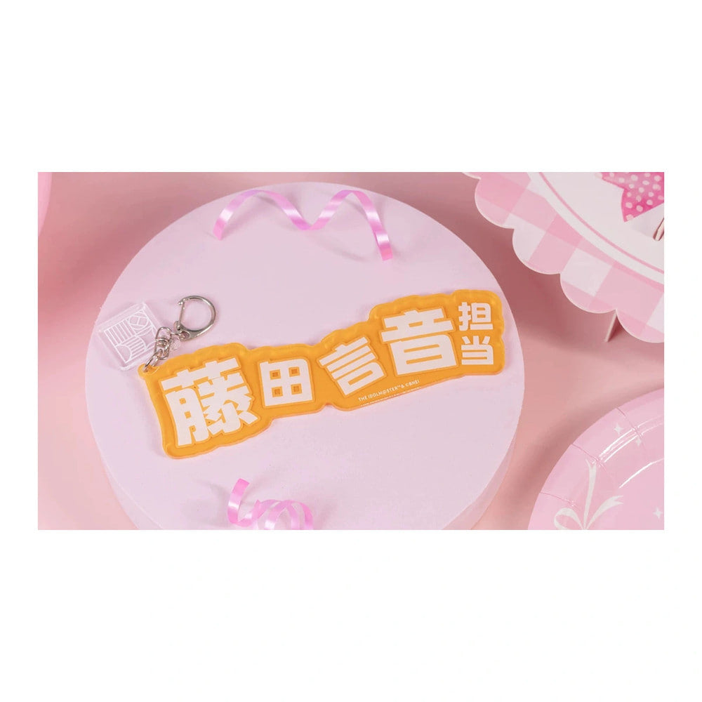 Name keychain: orange-yellow plate reading "藤田言音担当" in white, with a clasp and a small clear charm