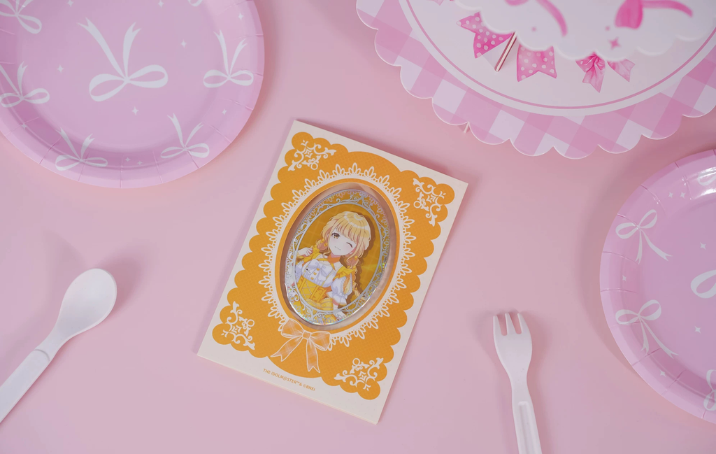 The Kotone Fujita badge on its backing card, photographed on a pink table with paper plate and cutlery props