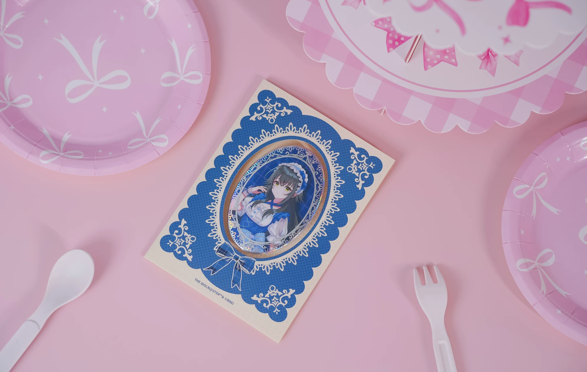 The Temari Tsukimura badge on its backing card, photographed on a pink table with paper plate and cutlery props
