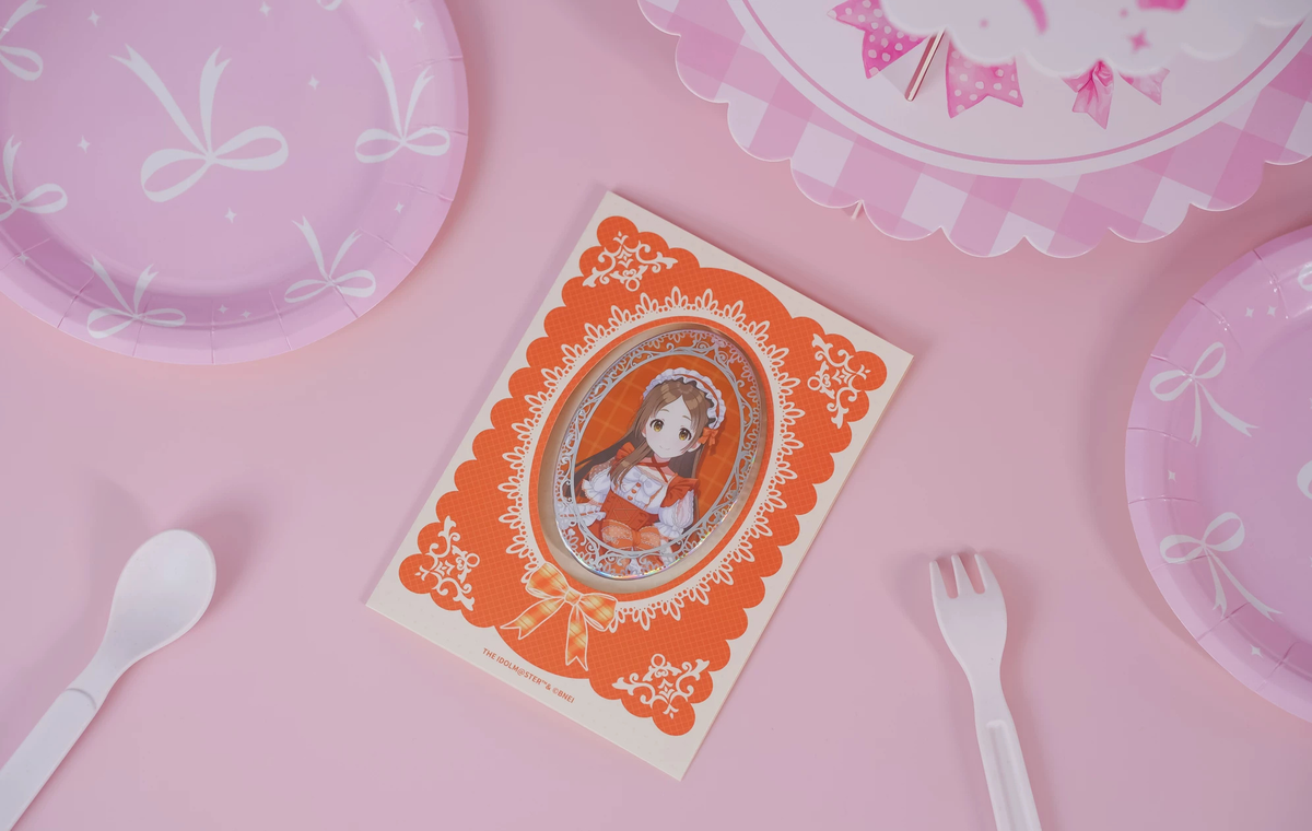 The China Kuramoto badge on its backing card, photographed on a pink table with paper plate and cutlery props