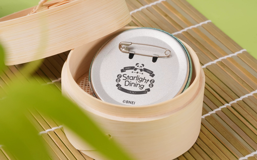 Back of a badge with a safety pin and the Starlight Dining 2026 logo, photographed in a bamboo steamer