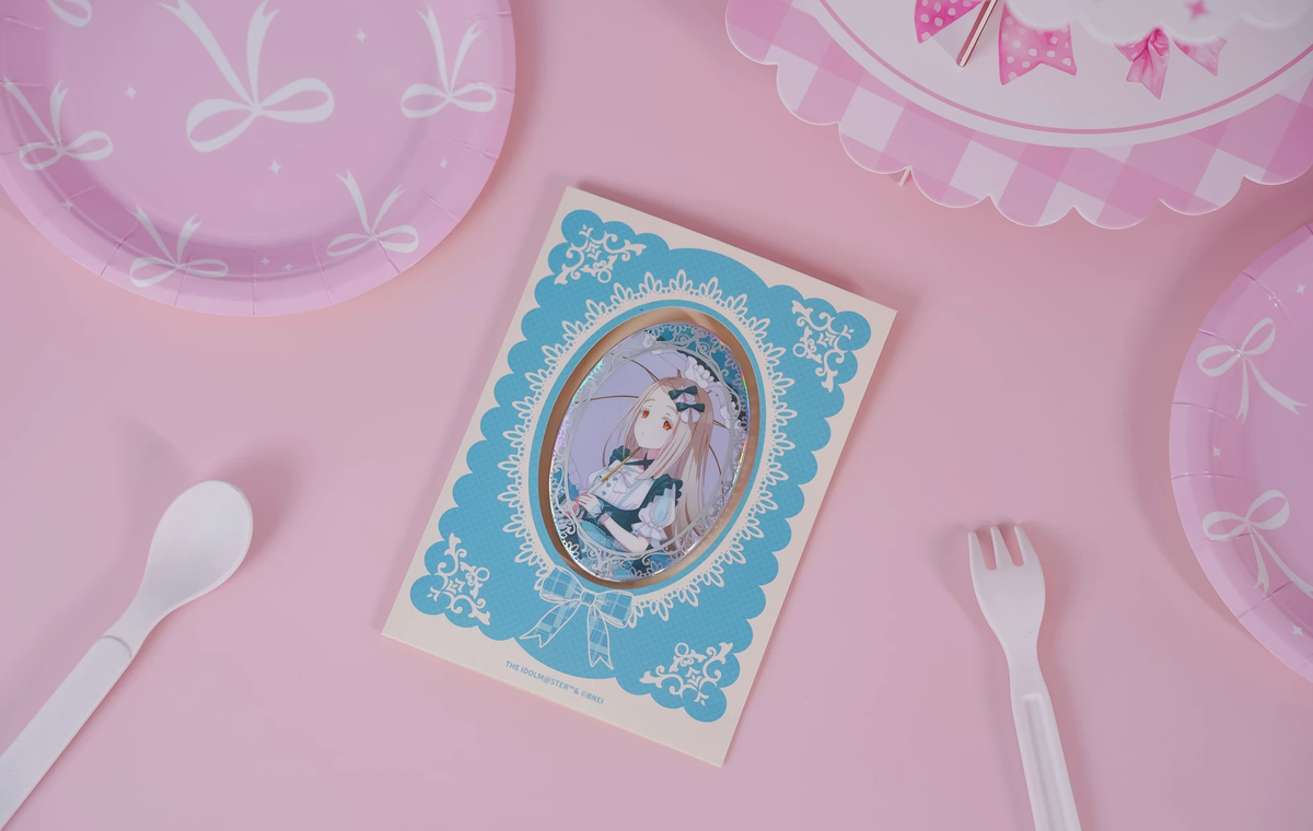 The Hiro Shinosawa badge on its backing card, photographed on a pink table with paper plate and cutlery props